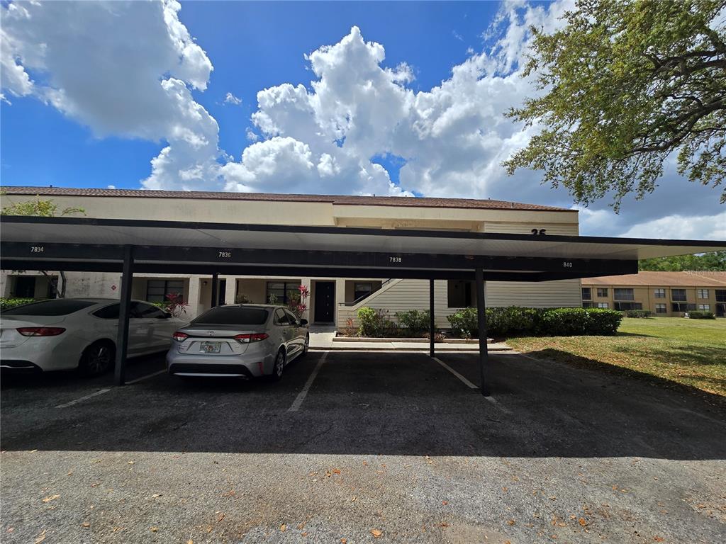 A covered parking structure sits in front of a two-story apartment building under a cloudy sky — 7838 NIAGARA AVENUE UNIT 305, TAMPA, FL