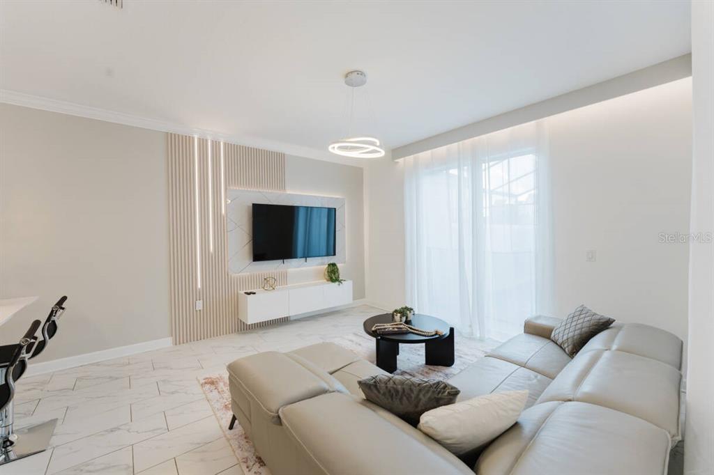 A modern living room features a wall-mounted television, slatted wood accents, and a leather sectional — 3017 PENELOPE LOOP, KISSIMMEE, FL