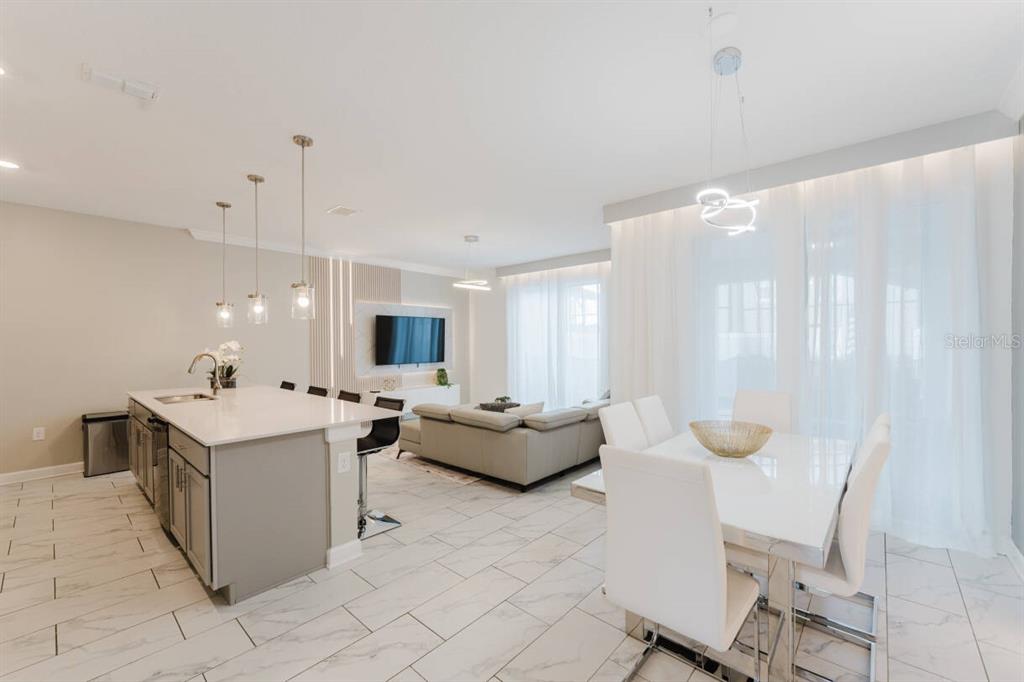 An open-concept kitchen, dining area, and living room featuring white tile floors and modern furniture — 3017 PENELOPE LOOP, KISSIMMEE, FL