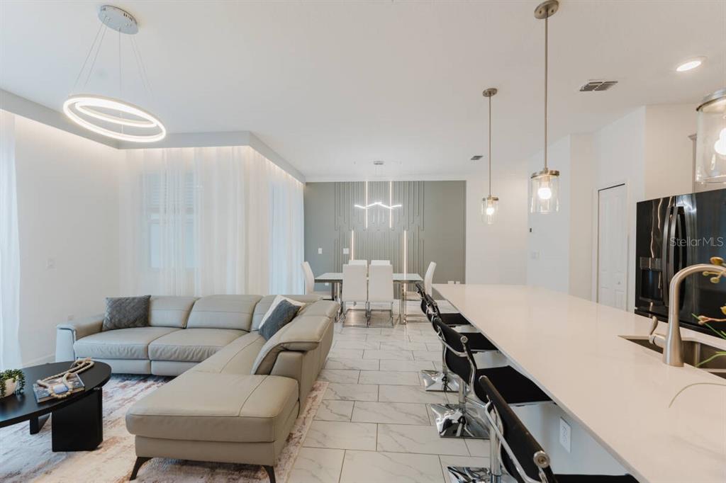 An open-concept living and dining area features a sectional sofa, kitchen island, and modern lighting — 3017 PENELOPE LOOP, KISSIMMEE, FL