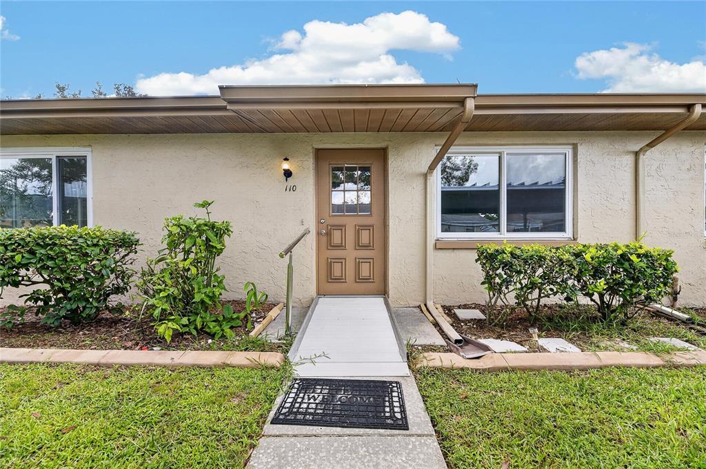 The exterior of a single-story home features a tan facade, a brown door, and a ramp — 110 GLOUCESTER BOULEVARD UNIT 346, SUN CITY CENTER, FL