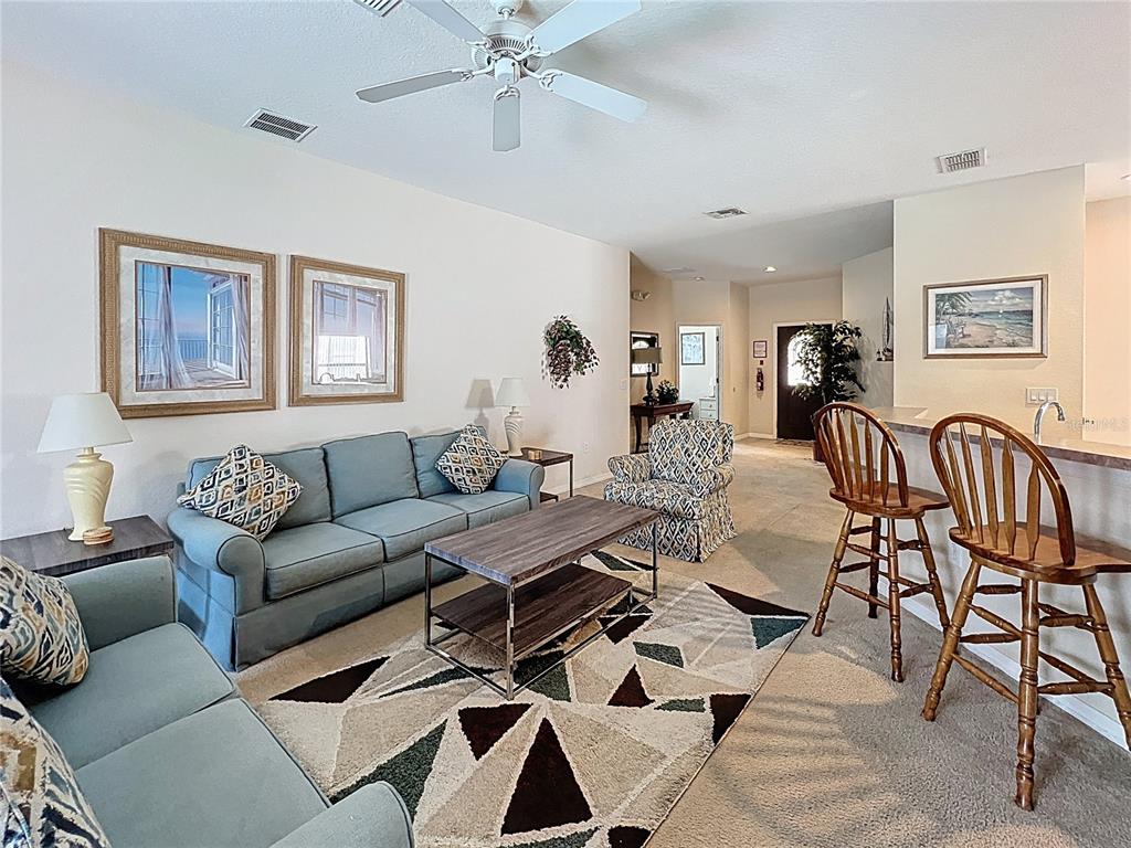 A living room features a blue sofa, patterned armchair, wooden coffee table, and bar stools — 102 SANDY POINT WAY, CLERMONT, FL