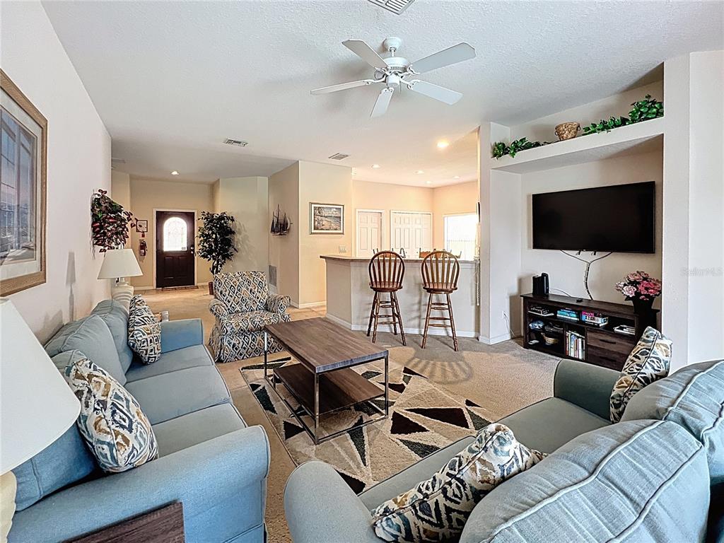 A living room features a blue sofa, a patterned rug, and a television mounted above a console — 102 SANDY POINT WAY, CLERMONT, FL