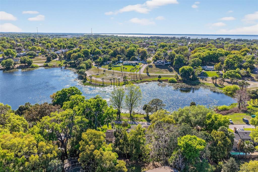 An aerial view shows a lake surrounded by trees and residential houses under a blue sky — 1039 LAKE GRACIE DRIVE, EUSTIS, FL