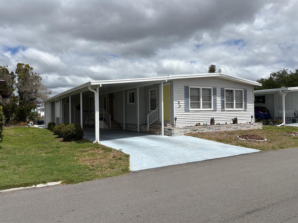 A single-story manufactured home with light siding, a carport, and a yellow front door — 413 CERVINA DRIVE N, VENICE, FL