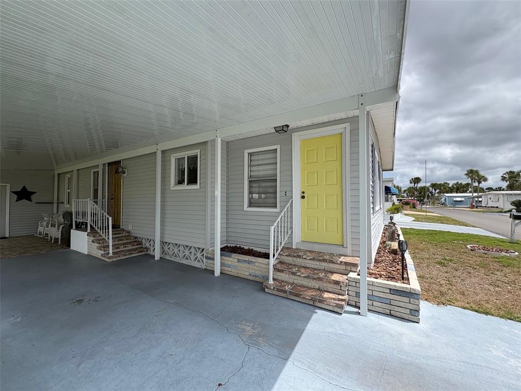 A mobile home exterior features a yellow front door, a carport, and stone-tiled steps — 413 CERVINA DRIVE N, VENICE, FL