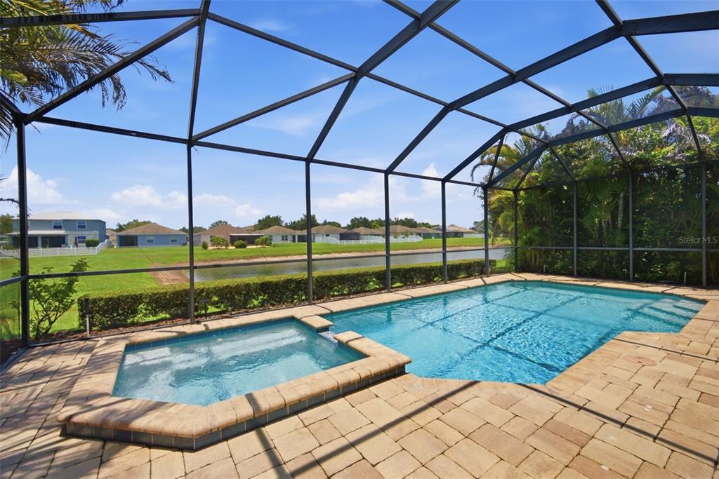 A screened-in pool and spa with paver decking overlooking a pond and residential neighborhood — 11432 DRIFTING LEAF DRIVE, RIVERVIEW, FL
