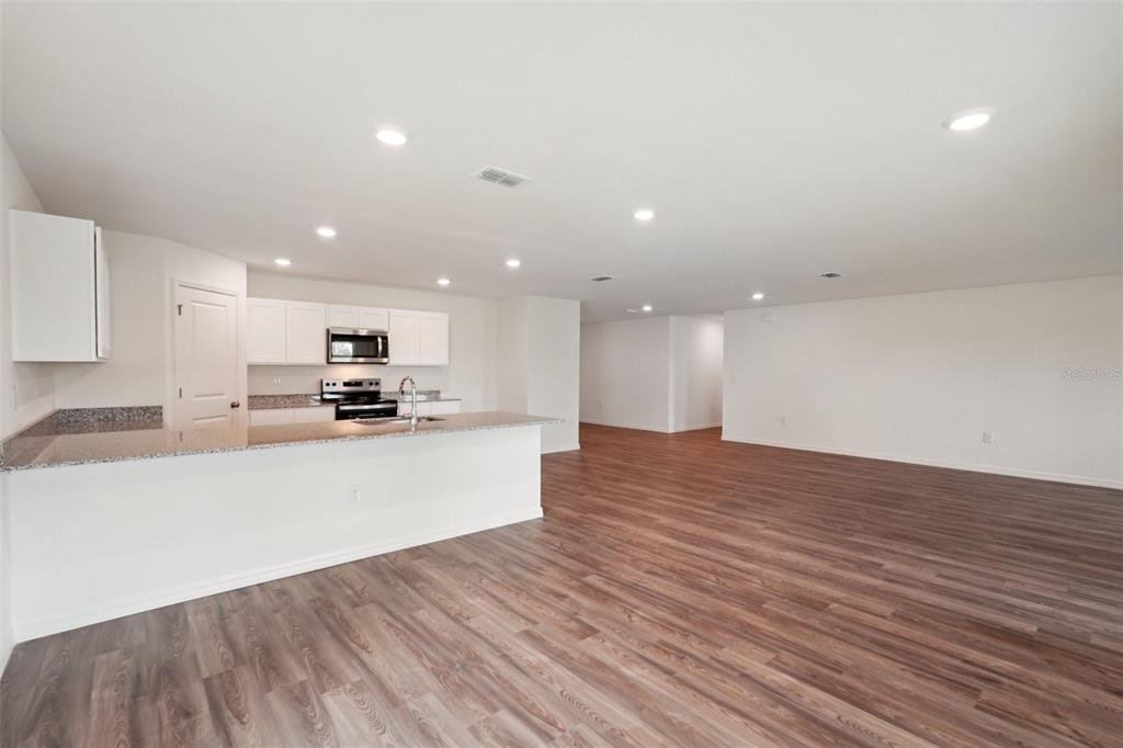An open-concept kitchen and living area features white cabinets, granite countertops, and wood-look flooring — 11230 HORNED OWL ROAD, WEEKI WACHEE, FL