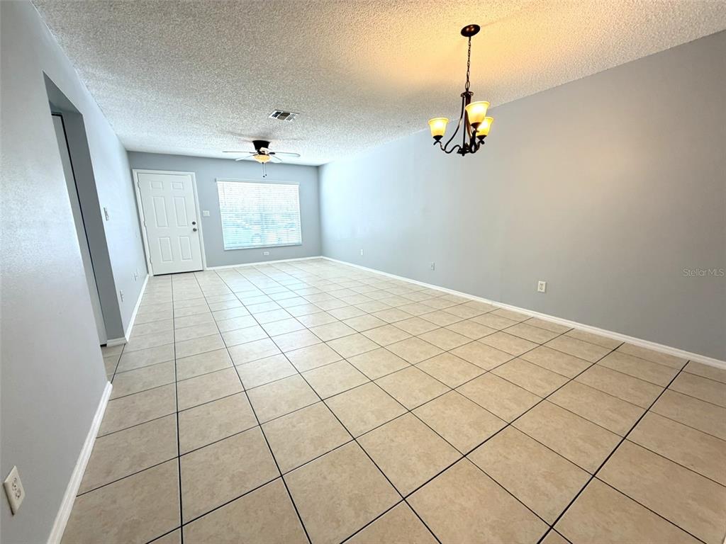 An empty room features light gray walls, beige tiled flooring, a ceiling fan, and a chandelier — 546 PIGEON CIRCLE, ORLANDO, FL