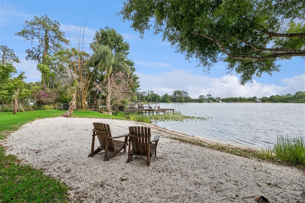 Two wooden chairs sit on a sandy beach overlooking a lake with a wooden dock — 9642 BEAR LAKE ROAD, APOPKA, FL