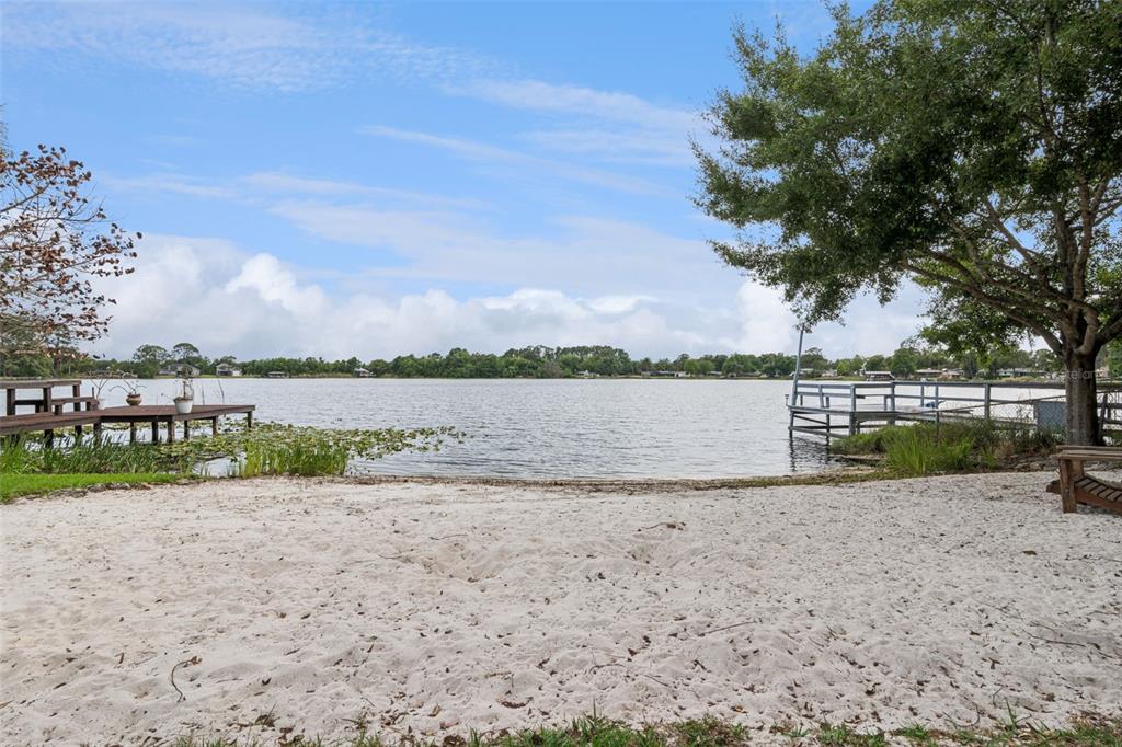A sandy beach area overlooks a lake with two wooden docks and a large tree — 9642 BEAR LAKE ROAD, APOPKA, FL