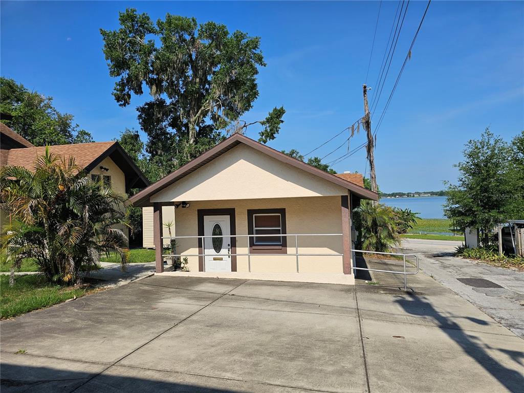 A small, light-colored house with a concrete driveway, metal railings, and a lake in back — 737 W CENTRAL AVENUE, WINTER HAVEN, FL