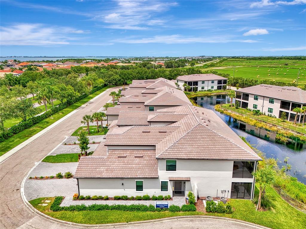 An aerial view shows a multi-unit residential building with a tiled roof beside a pond — 5632 SUMMIT POINTE CIRCLE UNIT 104, BRADENTON, FL