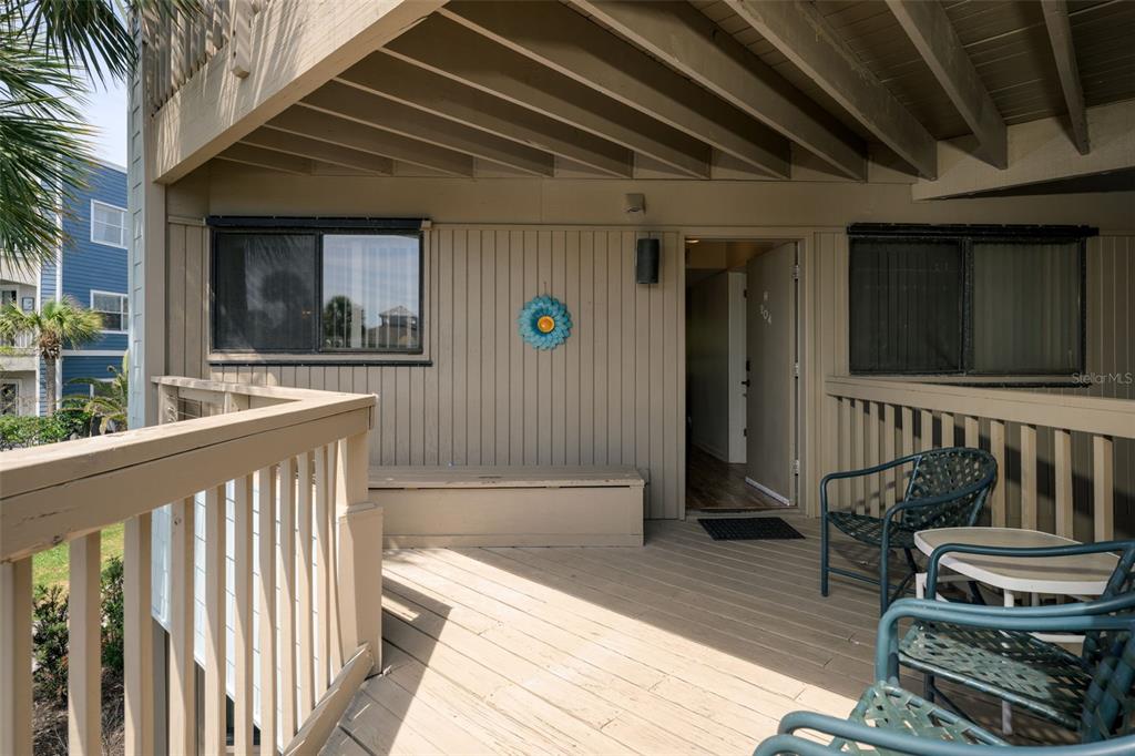 A wooden deck features a bench, patio furniture, and an open doorway to a unit — 130 OCEAN HIBISCUS DRIVE UNIT 204, ST AUGUSTINE, FL