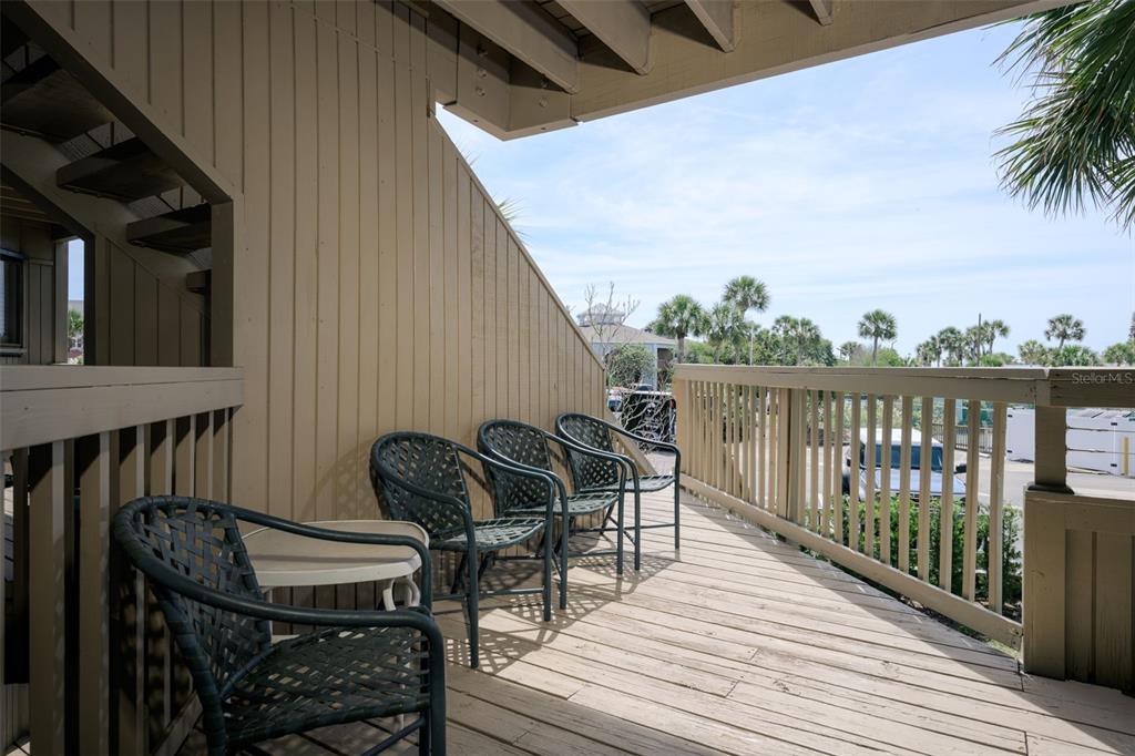 A wooden balcony features four dark metal chairs and a small table overlooking a parking lot — 130 OCEAN HIBISCUS DRIVE UNIT 204, ST AUGUSTINE, FL