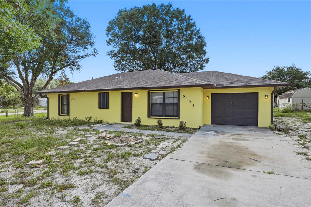 A yellow single-story house features a brown roof, a garage, and a concrete driveway — 5377 BECK DRIVE, COCOA, FL