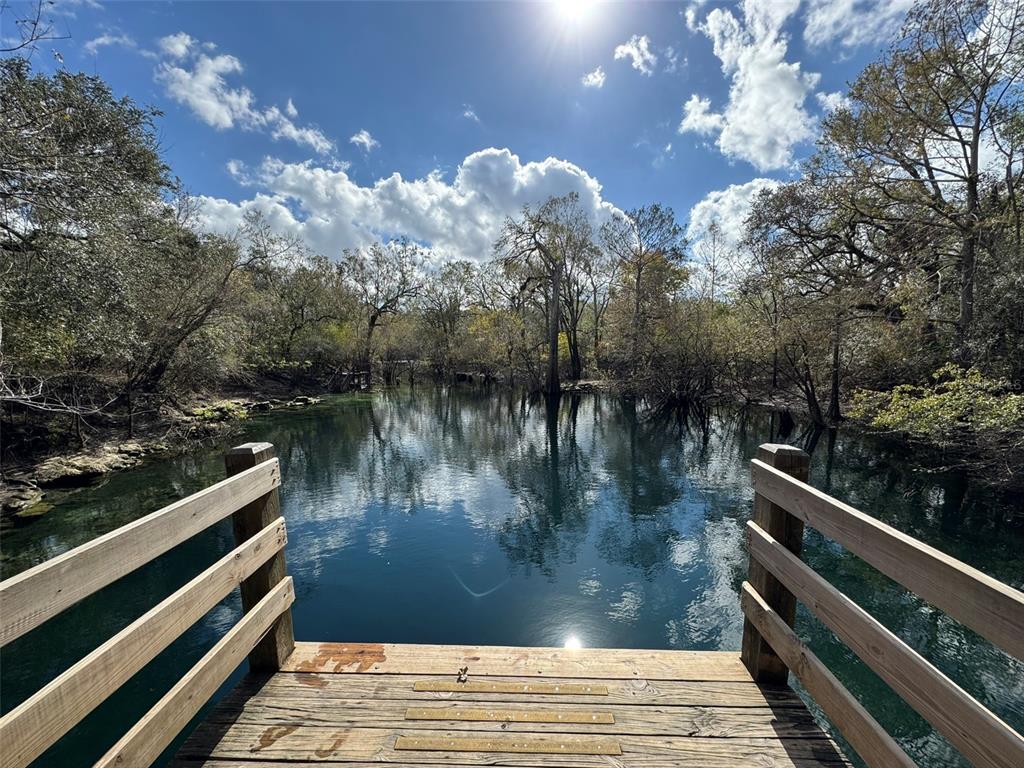 A wooden observation deck overlooks a calm, clear spring surrounded by trees under a sunny sky — 143RD DRIVE, O'BRIEN, FL