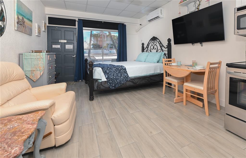 A studio apartment features a bed, dining set, kitchenette, and a beige recliner on tile — 18399 GULF BOULEVARD UNIT 367, INDIAN SHORES, FL