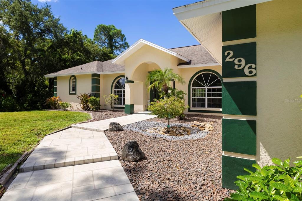 A beige house exterior features a stone walkway, gravel landscaping, and dark green accent pillars — 296 PINE RANCH TRAIL, OSPREY, FL
