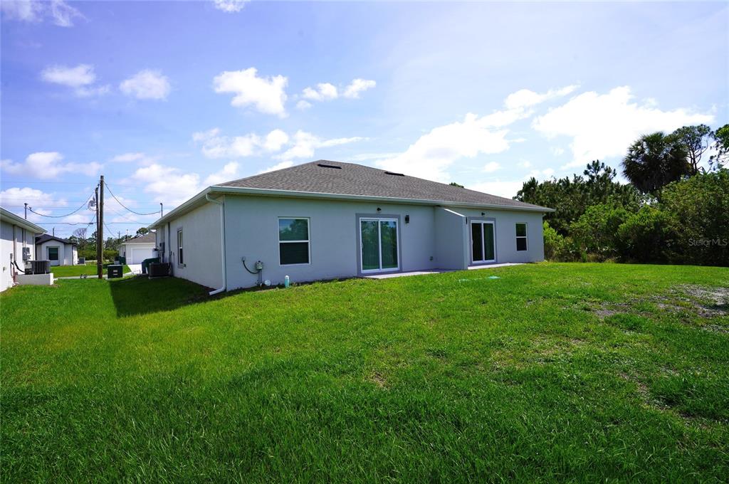 The rear exterior of a light-colored house features a sliding glass door and green lawn — 12032 TETZEL AVENUE, PORT CHARLOTTE, FL