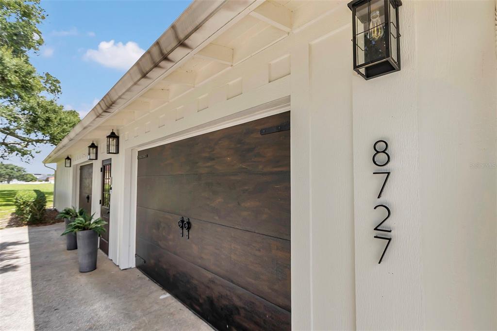 A side view of a house exterior featuring a dark wood garage door and address numbers — 8727 SE 72ND AVENUE, OCALA, FL