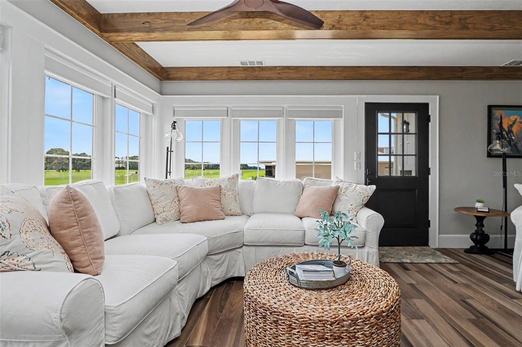A living room features a white sectional sofa, a round woven coffee table, and wood-beamed ceilings — 8727 SE 72ND AVENUE, OCALA, FL