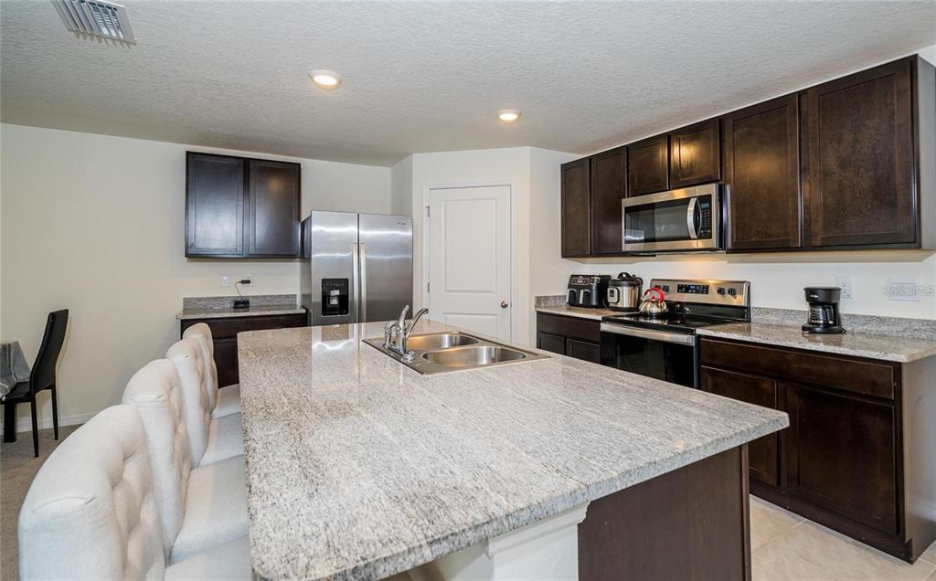 A kitchen with dark wood cabinets, granite countertops, a large island, and stainless steel appliances — 7590 BROAD POINTE DRIVE, ZEPHYRHILLS, FL