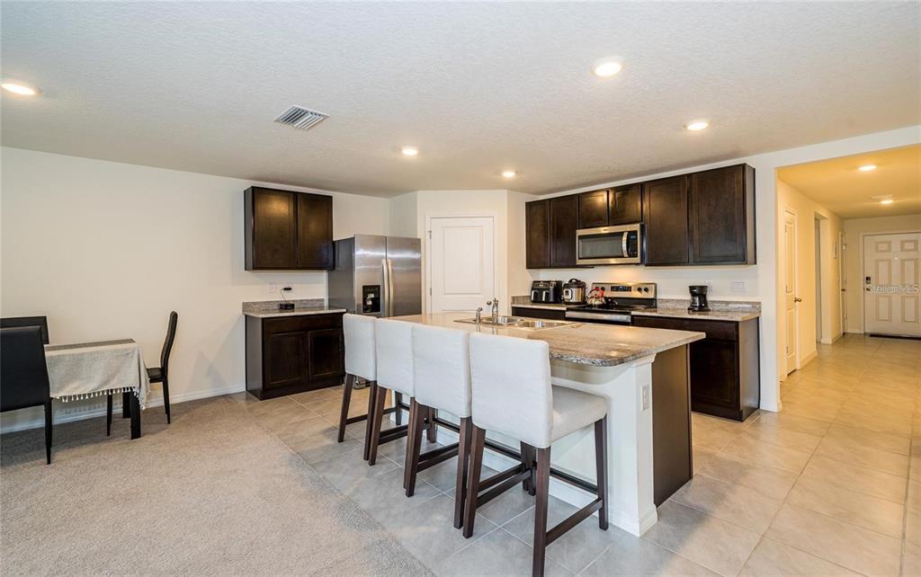 A kitchen features dark wood cabinets, granite countertops, a center island, and tile flooring — 7590 BROAD POINTE DRIVE, ZEPHYRHILLS, FL