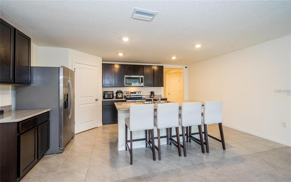 A kitchen features dark wood cabinets, granite countertops, a center island, and four bar stools — 7590 BROAD POINTE DRIVE, ZEPHYRHILLS, FL