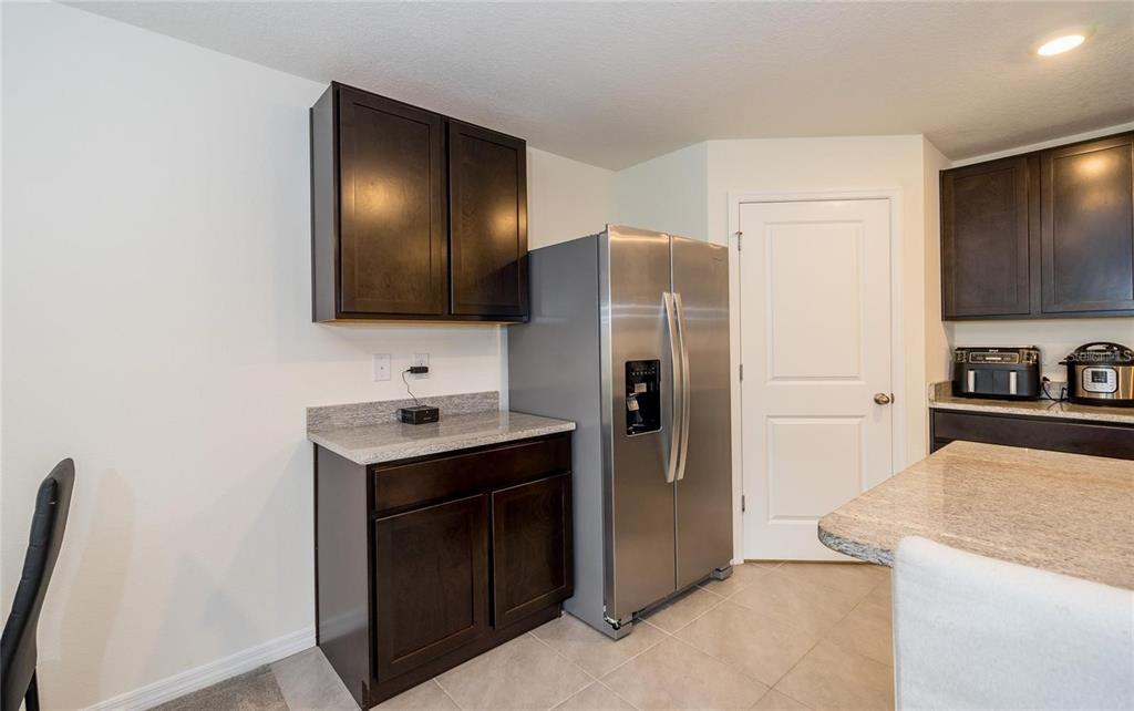 A kitchen features dark wood cabinets, granite countertops, and a stainless steel refrigerator — 7590 BROAD POINTE DRIVE, ZEPHYRHILLS, FL