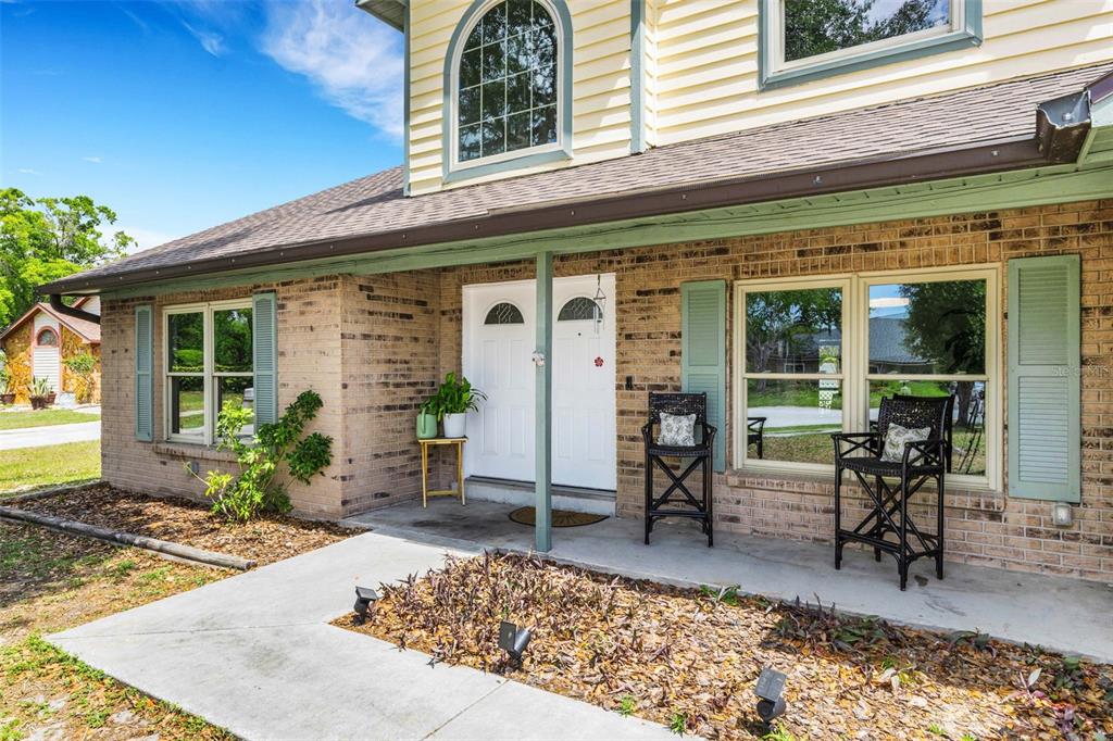 A brick house exterior features a covered porch with two white doors and black chairs — 4304 LUKOW PLACE, VALRICO, FL