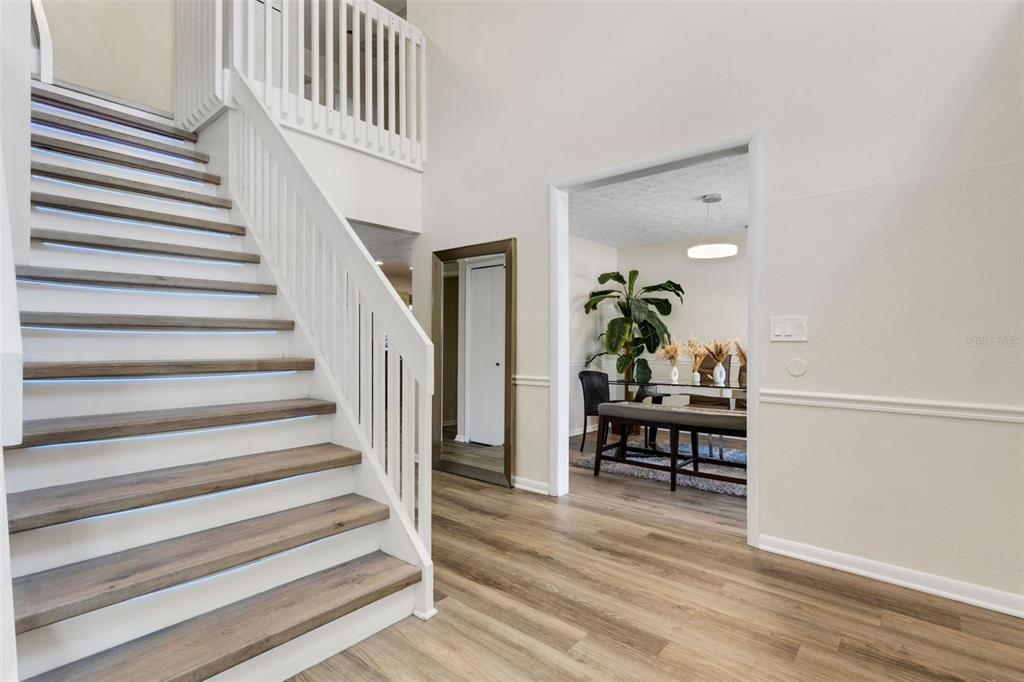 A staircase with wood treads and white railings leads to a landing near a dining room — 4304 LUKOW PLACE, VALRICO, FL