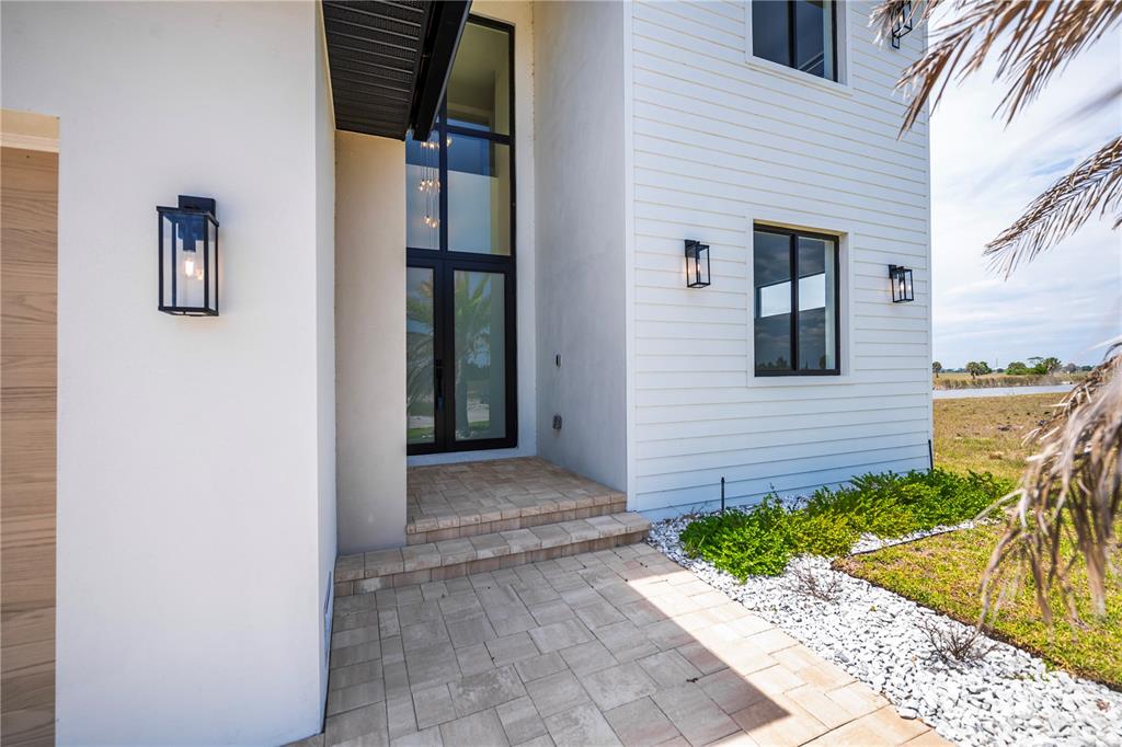 The exterior of a modern house features a tall glass entryway, white siding, and pavers — 7 SUNFLOWER DRIVE, PLACIDA, FL