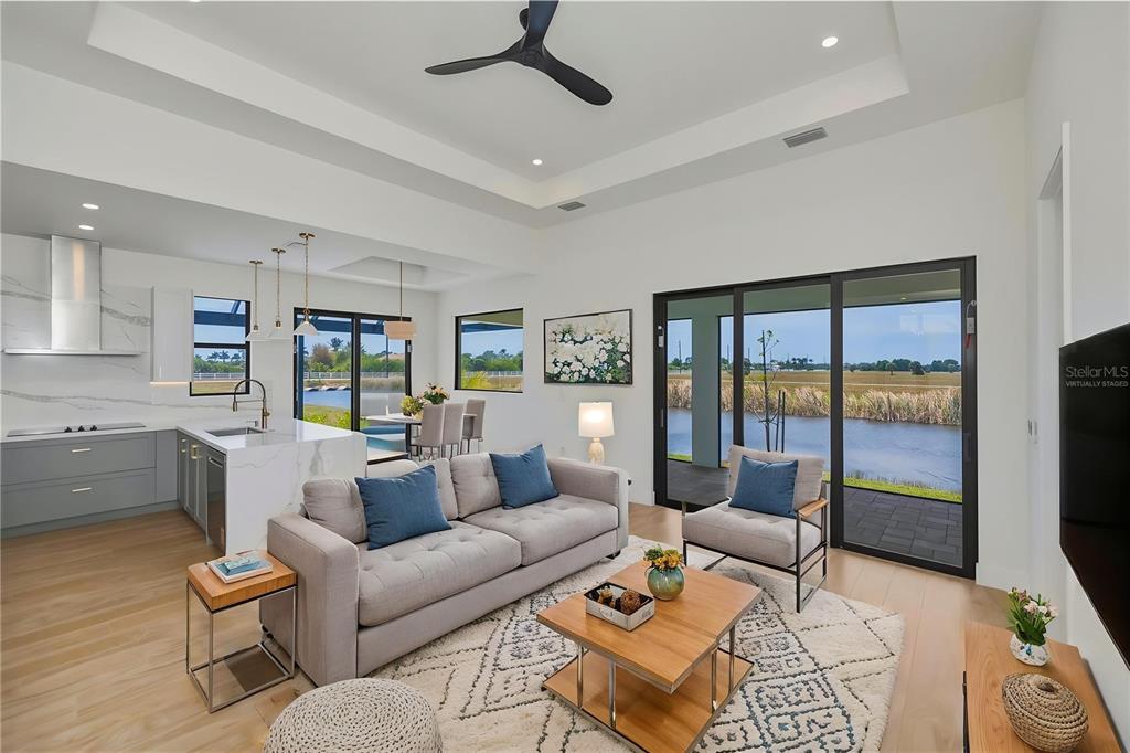 A modern open-concept living room and kitchen overlook a backyard pond through sliding glass doors — 7 SUNFLOWER DRIVE, PLACIDA, FL