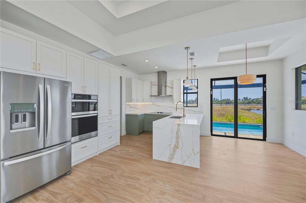 A modern kitchen features white cabinetry, a marble-topped island, and sliding glass doors overlooking a pool — 7 SUNFLOWER DRIVE, PLACIDA, FL