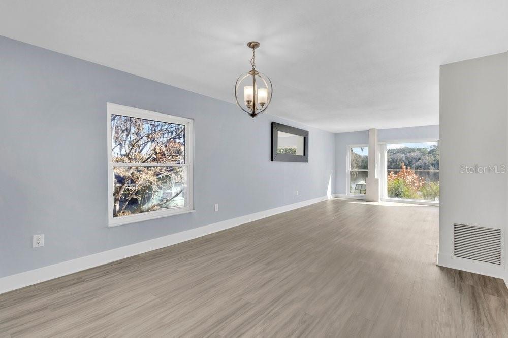 An empty living room with light blue walls, wood-look flooring, and a round chandelier — 6670 BAY SHORE DRIVE, ST CLOUD, FL