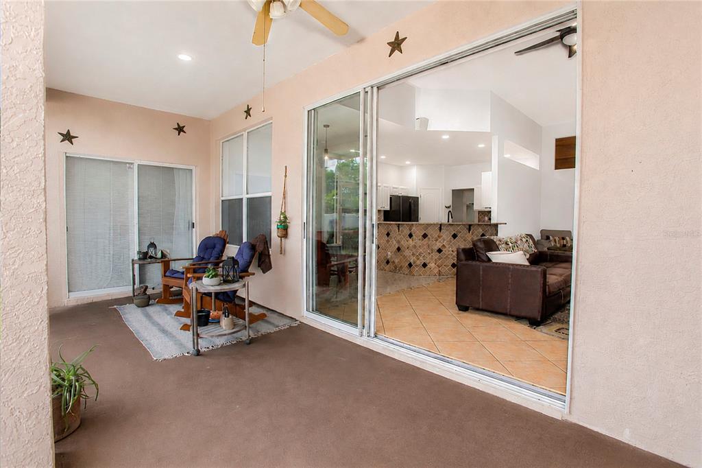 A covered patio with two rocking chairs overlooks an interior living area and kitchen — 3307 ROYAL ASCOT RUN, GOTHA, FL