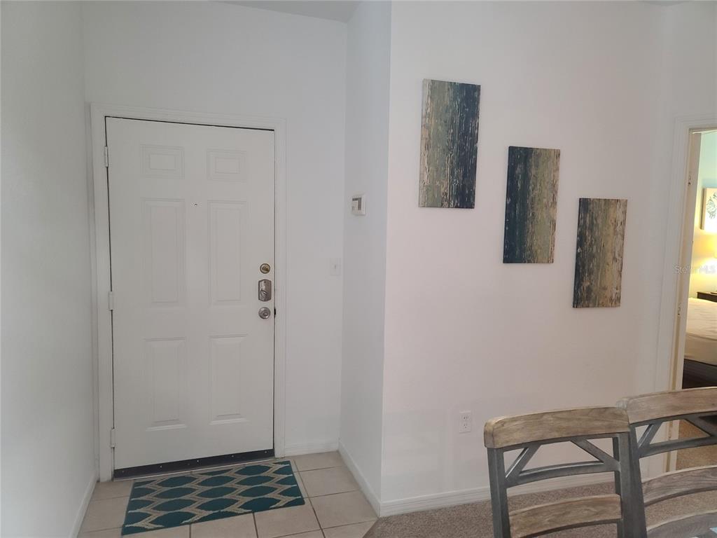 An entryway features a white door, tiled floor, and three abstract paintings on the wall — 8908 LEGACY COURT UNIT 16-104, KISSIMMEE, FL