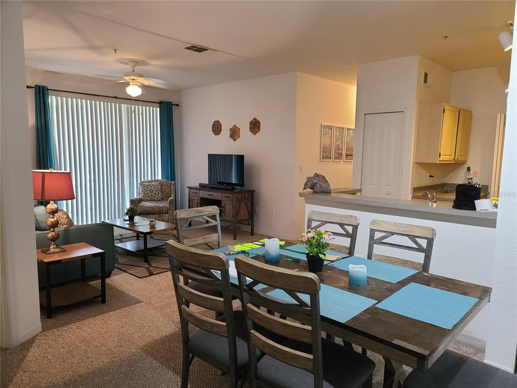 An open-concept living and dining area features a wooden table, sofa, and kitchen pass-through — 8908 LEGACY COURT UNIT 16-104, KISSIMMEE, FL