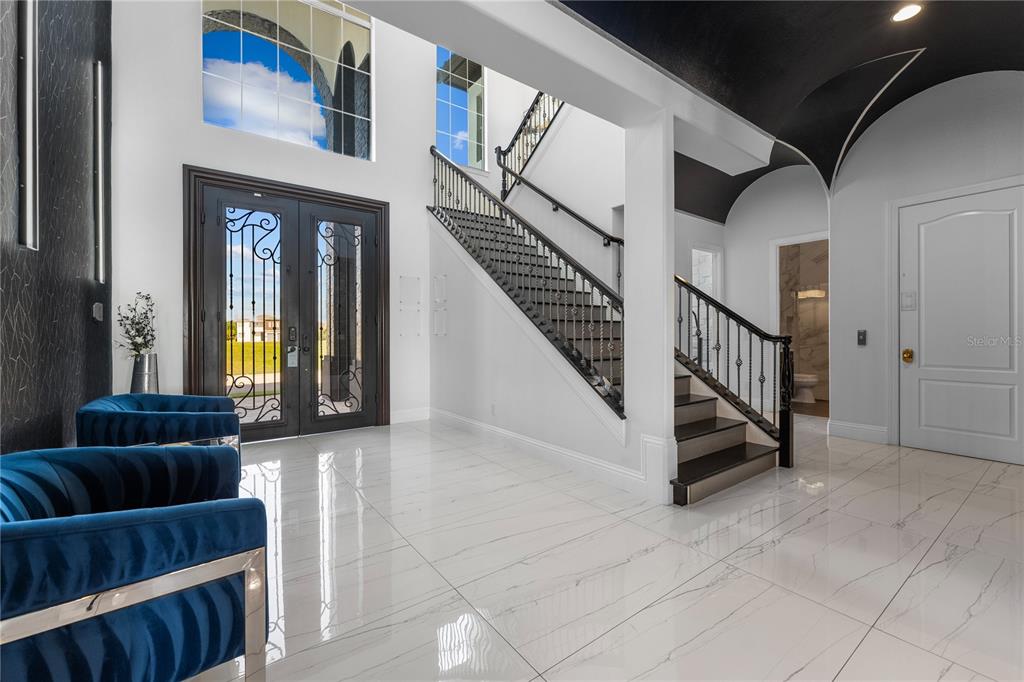 A grand foyer features white marble floors, a dark staircase, and blue velvet chairs — 1125 GRAND TRAVERSE PARKWAY, REUNION, FL