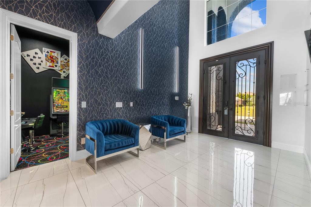 A modern entryway features blue velvet chairs, patterned wallpaper, and a double iron front door — 1125 GRAND TRAVERSE PARKWAY, REUNION, FL