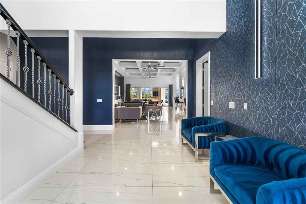 A foyer with white tile floors, a staircase, and blue velvet chairs leads to a living room — 1125 GRAND TRAVERSE PARKWAY, REUNION, FL