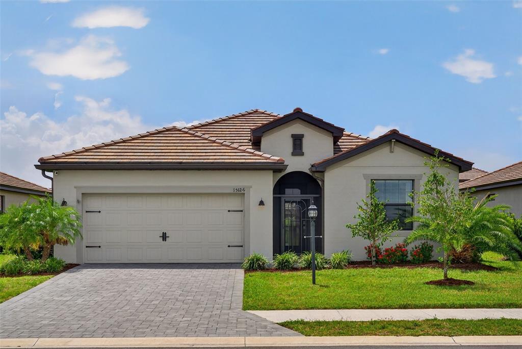 A single-story house with a beige stucco exterior, a tiled roof, and a paved driveway — 15126 MISTY WATER CROSSING, BRADENTON, FL