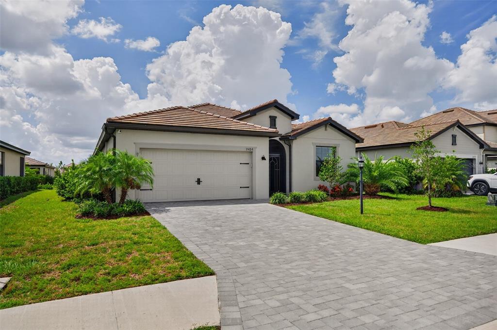 A single-story house with a tiled roof, beige stucco exterior, and a paved driveway — 15126 MISTY WATER CROSSING, BRADENTON, FL