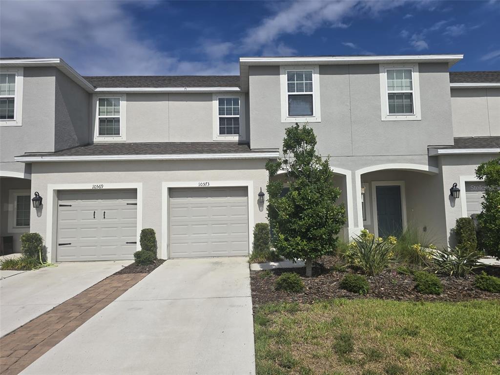 A two-story townhouse exterior features gray stucco walls, two garage doors, and a small lawn — 10573 OAKSIDE DRIVE, PALMETTO, FL