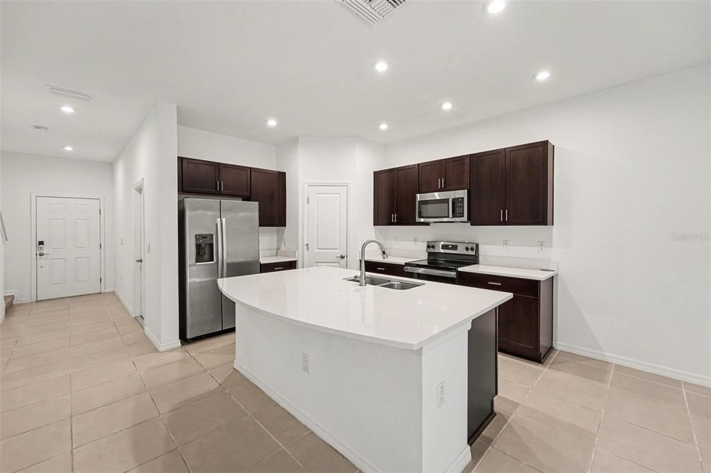 A modern kitchen features dark wood cabinets, white countertops, a center island, and stainless appliances — 10573 OAKSIDE DRIVE, PALMETTO, FL