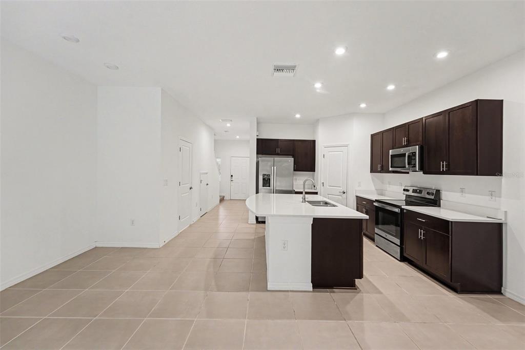 A modern kitchen features dark wood cabinets, a white island, and light tile flooring — 10573 OAKSIDE DRIVE, PALMETTO, FL