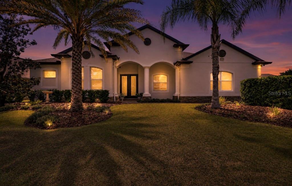 A single-story house with a stucco exterior, arched entryway, and palm trees at dusk — 8237 BRIDGEPORT BAY CIRCLE, MOUNT DORA, FL