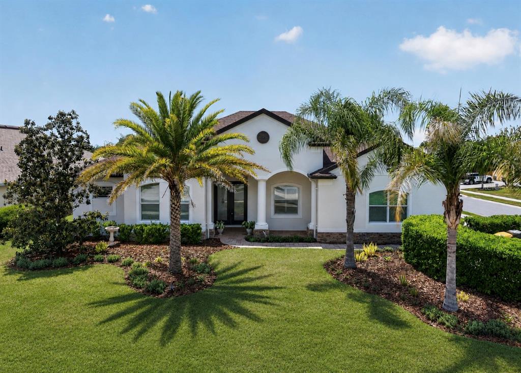 A single-story house with a white stucco facade, arched entryway, and two palm trees — 8237 BRIDGEPORT BAY CIRCLE, MOUNT DORA, FL