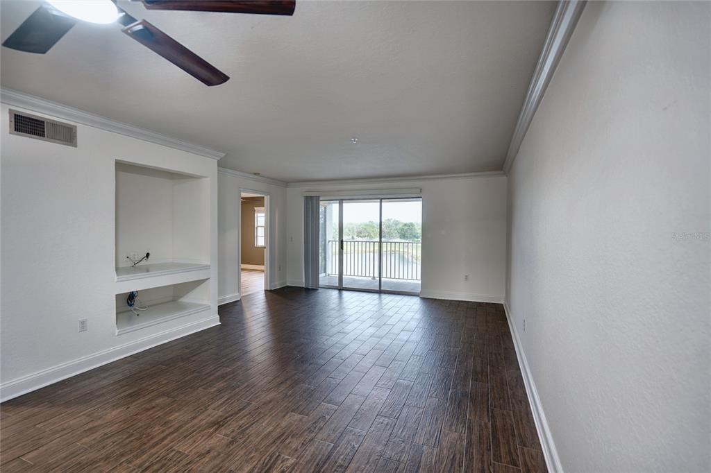 An empty living room features dark wood-look tile flooring, a built-in media niche, and a balcony — 13815 FAIRWAY ISLAND DRIVE UNIT 1335, ORLANDO, FL